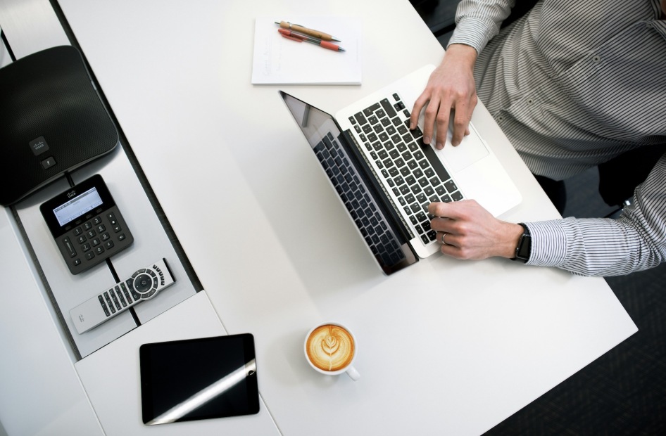 a person at a desk working on a laptop with a coffee pen and paper