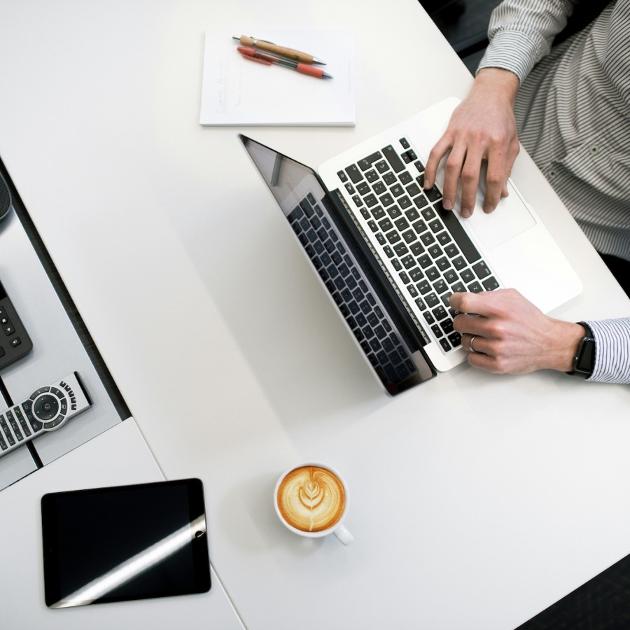 a person at a desk working on a laptop with a coffee pen and paper